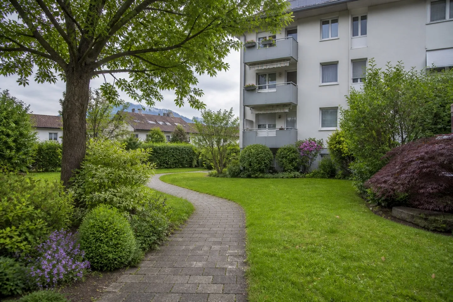 Saisonal gepflegte Grünanlage einer Wohnliegenschaft mit Rasen, Weg und Sträuchern